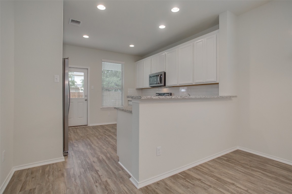 148 Spotted Rail Ridge Leander, TX 78641 - Photo 7 of 31 A contemporary kitchen space boasts bright white cabinetry and sleek stainless steel appliances, seamlessly integrating with wood-look flooring.