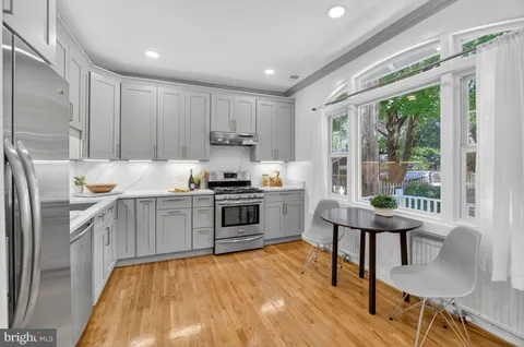 a kitchen with stainless steel appliances a stove a sink a refrigerator white cabinets and wooden floor