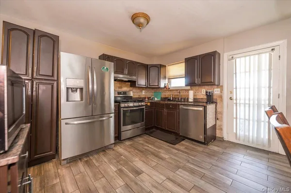 a kitchen with granite countertop stainless steel appliances a refrigerator cabinets and a wooden floor