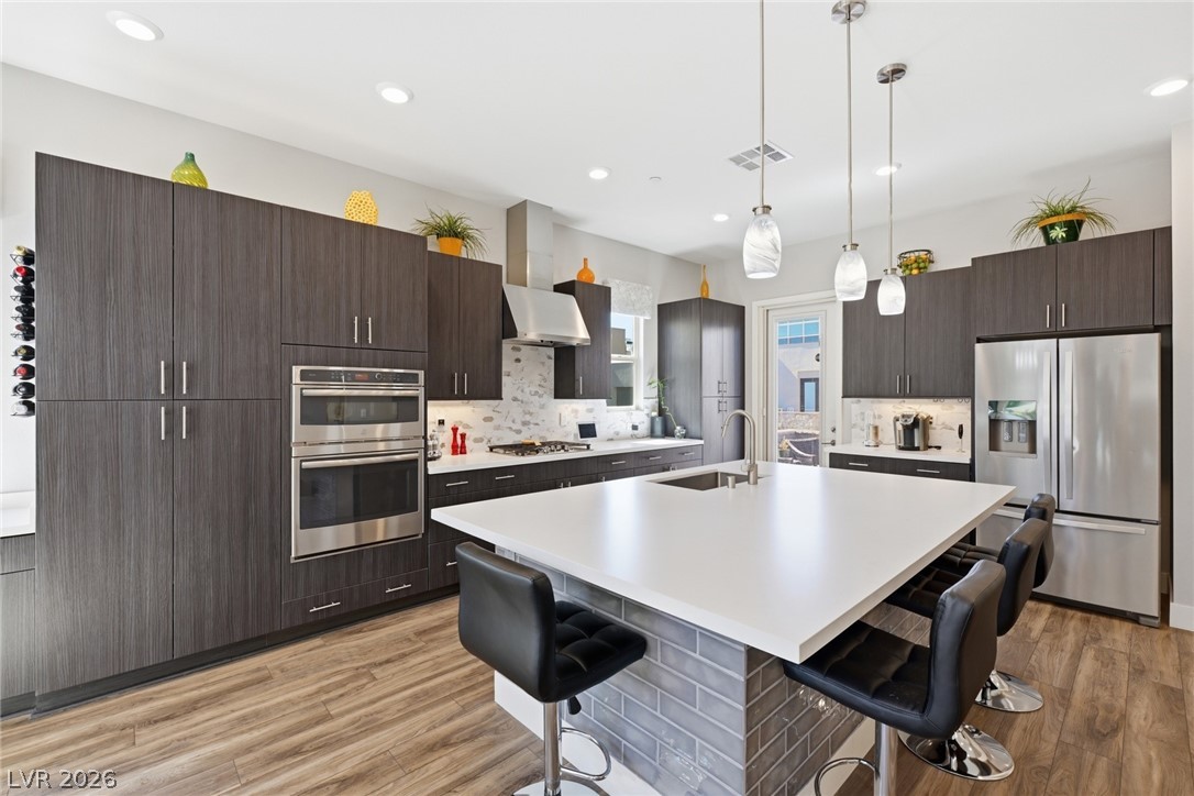 4246 Swift Street Las Vegas, NV 89135 - Photo 13 of 71 Kitchen featuring stainless steel appliances, a kitchen island with sink, dark wood finish cabinetry, light wood-style floors, and a breakfast bar area
