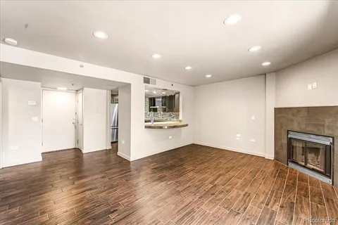 an empty room with wooden floor a fireplace and kitchen view
