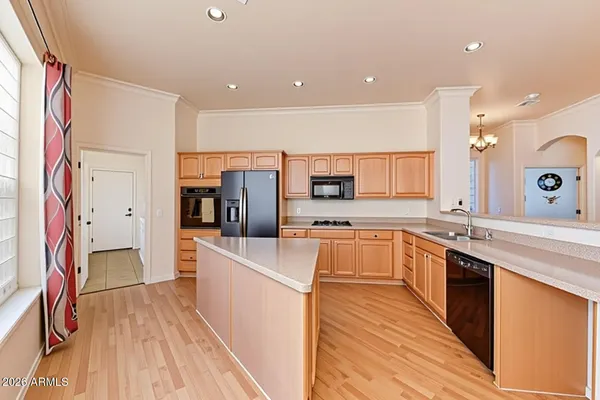 a large kitchen with stainless steel appliances a large counter top a stove a sink dishwasher and a refrigerator with wooden floor