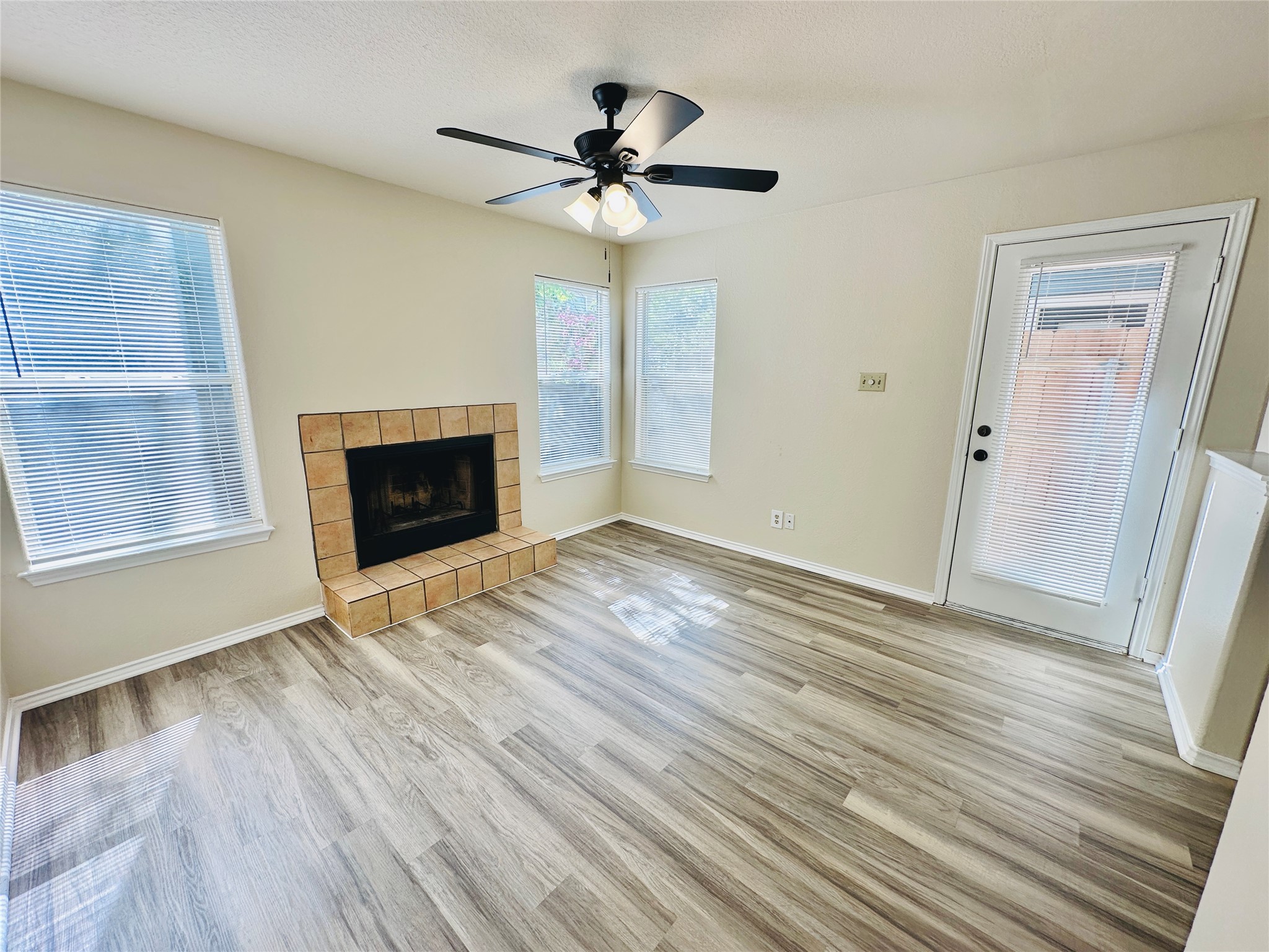8814 Schick Road, Unit C Austin, TX 78729 - Photo 8 of 35 Laminate flooring extends throughout this well-lit living room, featuring a tiled fireplace and a ceiling fan for comfort.