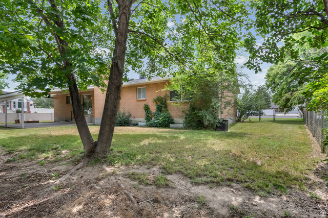 341 Heather Ridge Circle Sandy, UT 84070 - Photo 33 of 33 Expansive rear yard featuring mature trees, a brick exterior with white trim windows, and a covered patio area