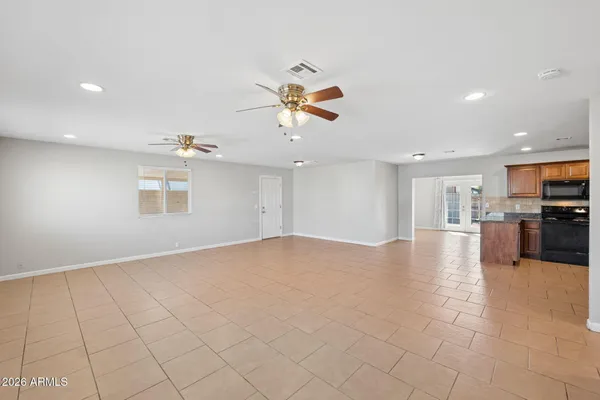 an empty room with kitchen view and a ceiling fan