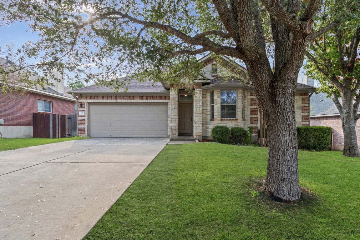View of front of house featuring concrete driveway, a front yard, an attached garage, a shingled roof, and stone siding