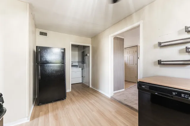 a view of a refrigerator in kitchen and an empty room with wooden floor
