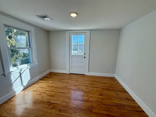 a view of an empty room with wooden floor and a window