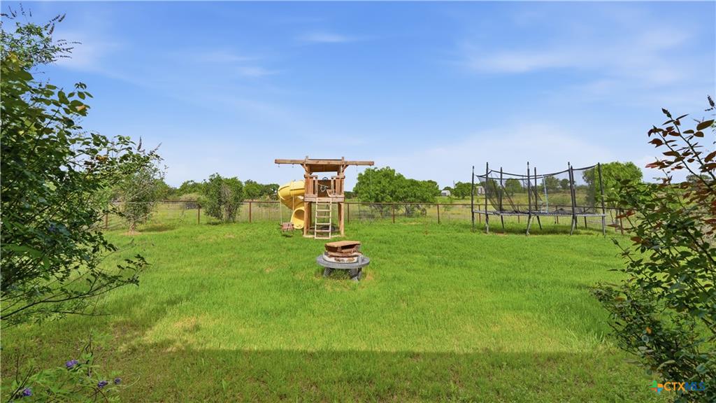127 Offer Llano, TX 78643 - Photo 38 of 40 Expansive backyard featuring a large green lawn, a wooden playset with a yellow slide, and a round fire pit with surrounding seating