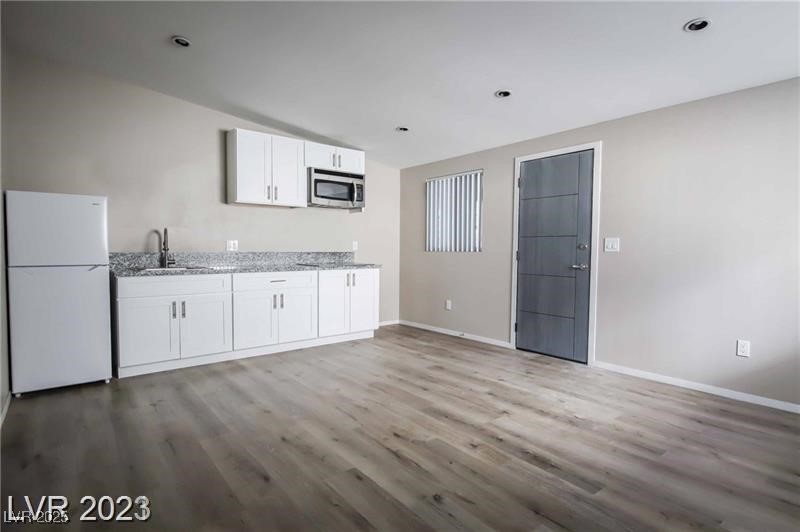 2201 Fairfield Avenue, Unit 9 Las Vegas, NV 89102 - Photo 6 of 7 Kitchen featuring freestanding refrigerator, light wood-type flooring, white cabinets, stainless steel microwave, and light stone countertops