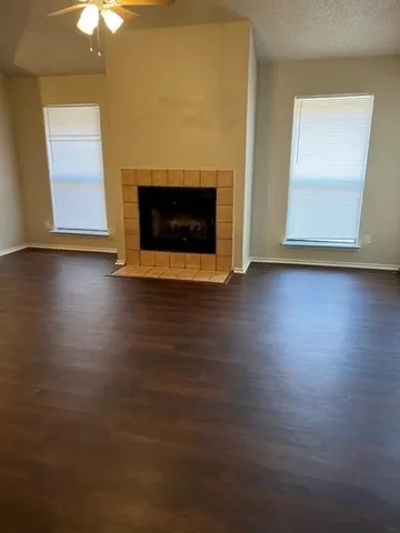 an empty room with wooden floor fire place and windows