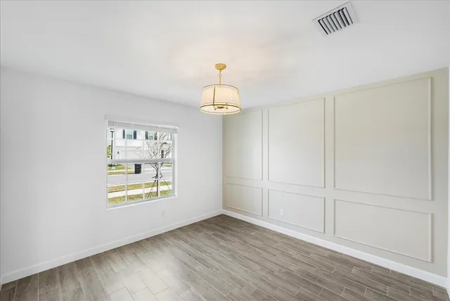 an empty room with wooden floor chandelier and windows