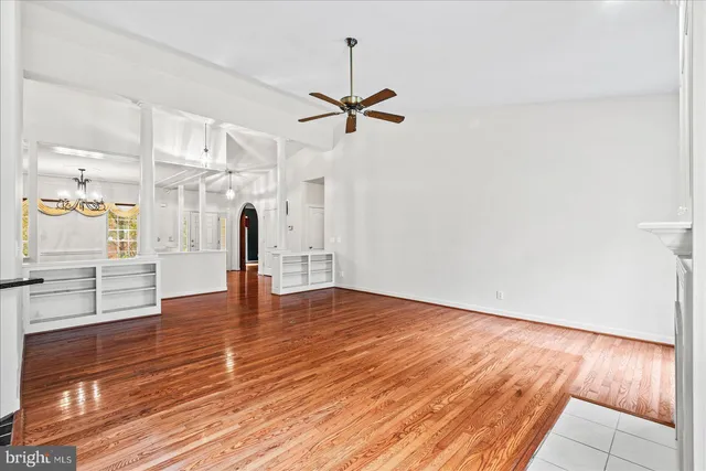 a view of an empty room with wooden floor and a ceiling fan