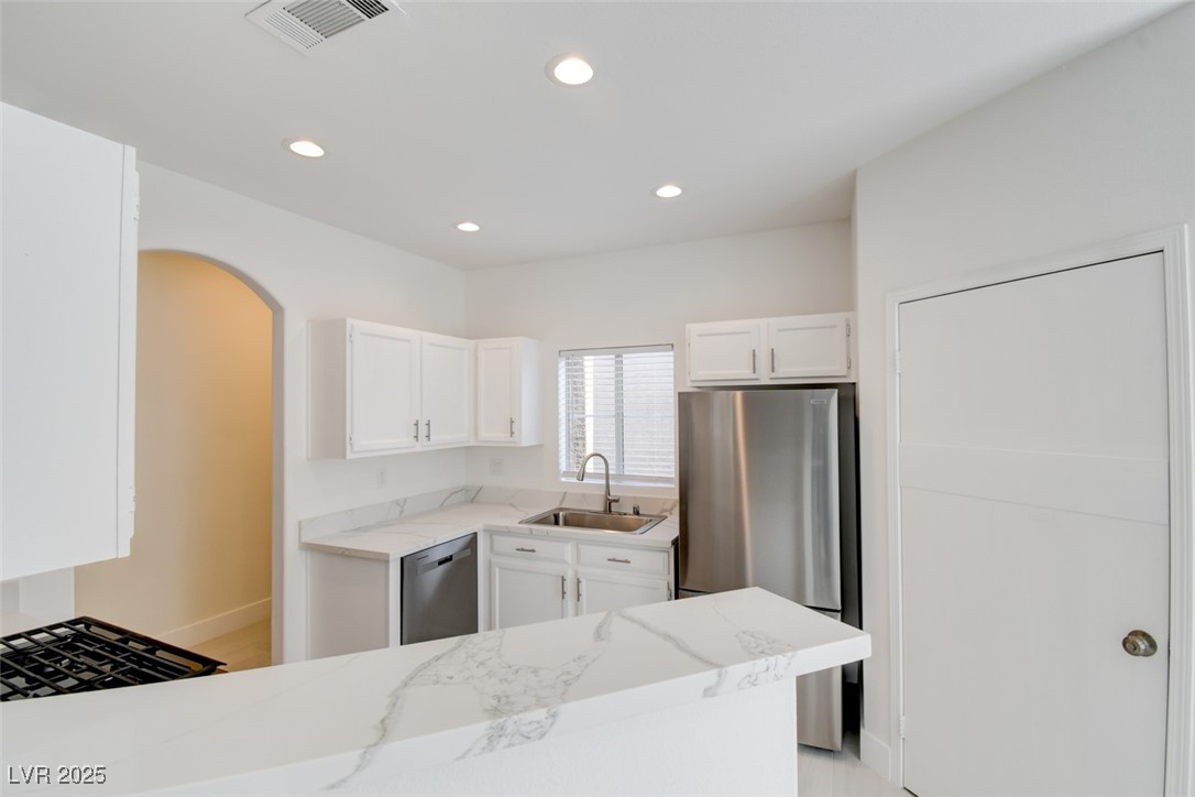 Kitchen featuring white cabinetry, appliances with stainless steel finishes, light stone counters, recessed lighting, and arched walkways