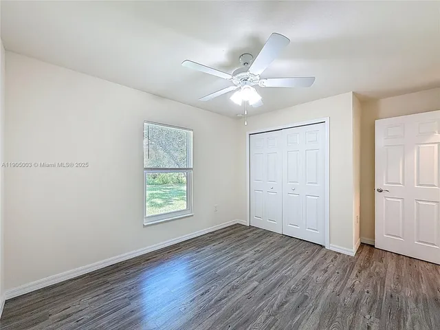 an empty room with wooden floor ceiling fan and windows