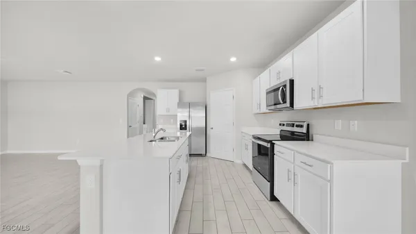 a large white kitchen with stainless steel appliances granite countertop a stove a sink dishwasher and a refrigerator with wooden floor