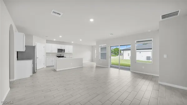 a view of an empty room with wooden floor and a kitchen