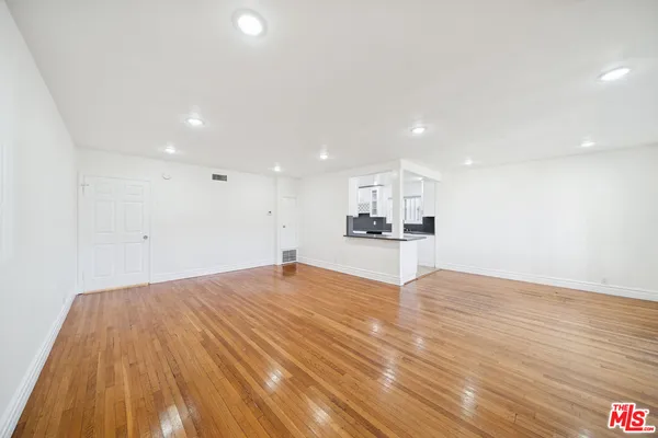 a view of kitchen and empty room with wooden floor