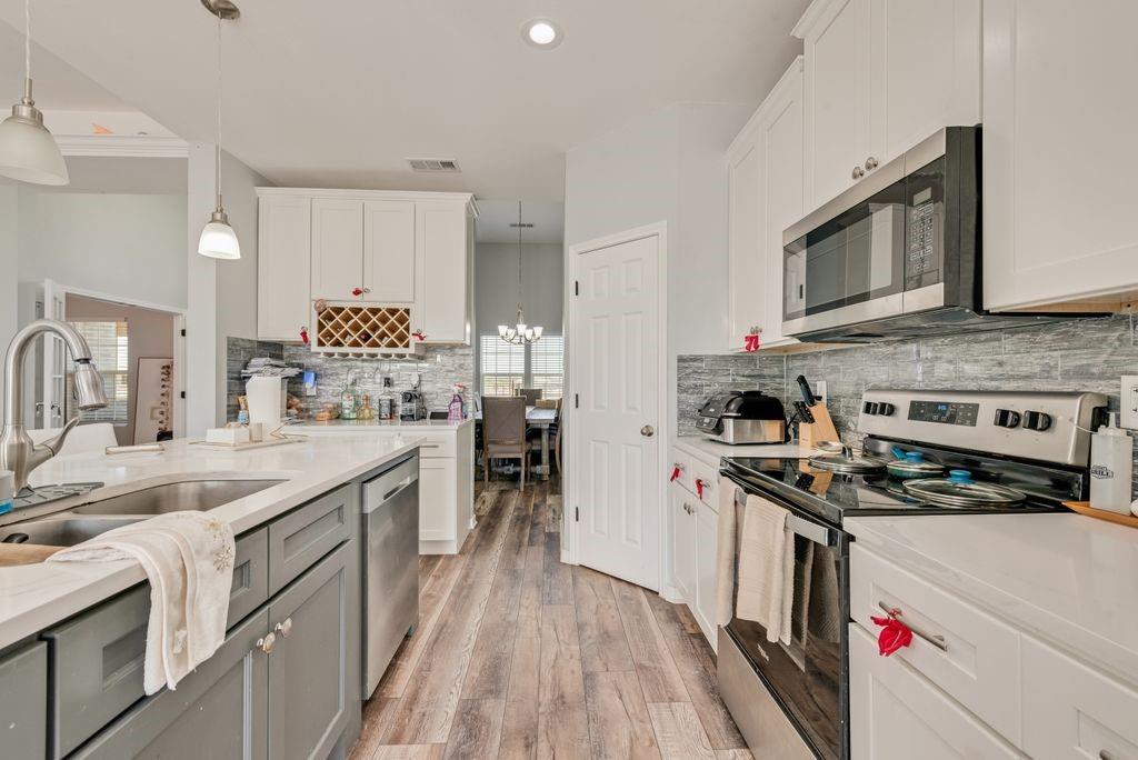 610 Ewing Road Ferris, TX 75125 - Photo 9 of 22 Kitchen featuring a center island with sink, white upper and gray lower cabinetry, stainless steel appliances, wood-finish flooring, and a tile backsplash
