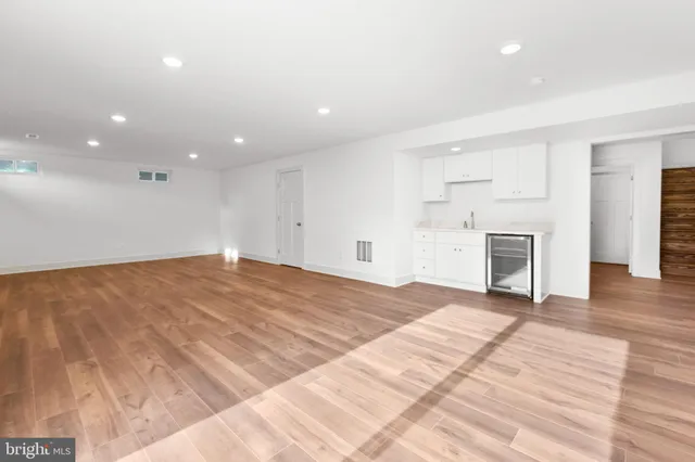 a view of an empty room with wooden floor and a kitchen