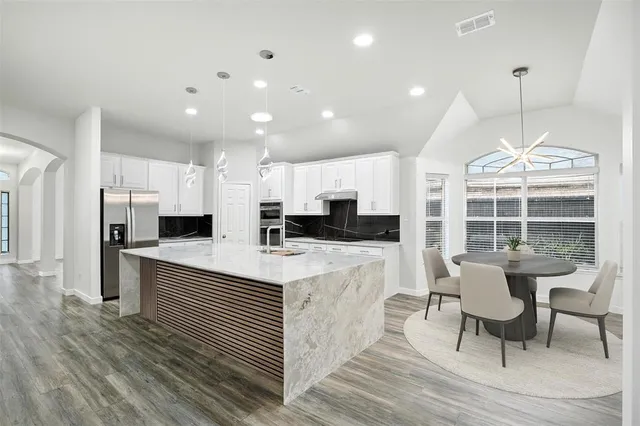 a kitchen with stainless steel appliances kitchen island granite countertop a table chairs and a refrigerator