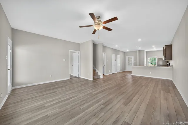 a view of an empty room with wooden floor and a ceiling fan