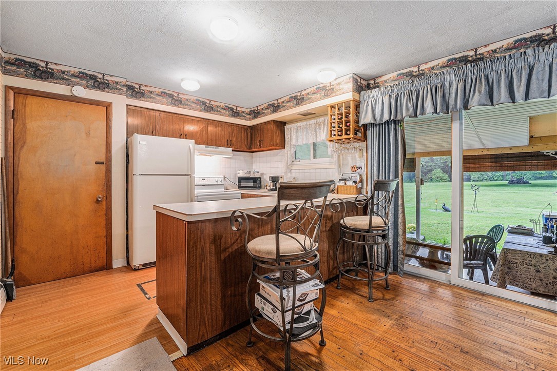 6315 Madison Road Thompson, OH 44086 - Photo 6 of 35 Kitchen featuring white appliances, under cabinet range hood, a peninsula, light wood-type flooring, and a textured ceiling