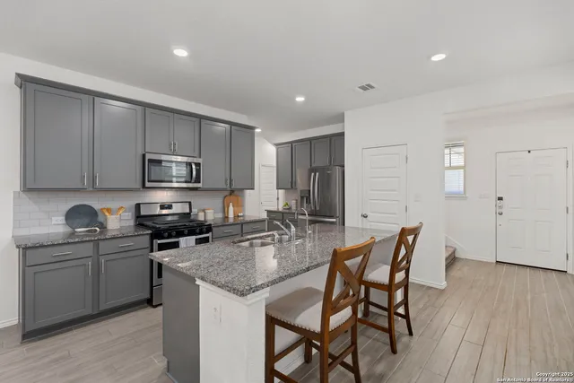 a kitchen with stainless steel appliances granite countertop a stove top oven a sink dishwasher a dining table and chairs with wooden floor