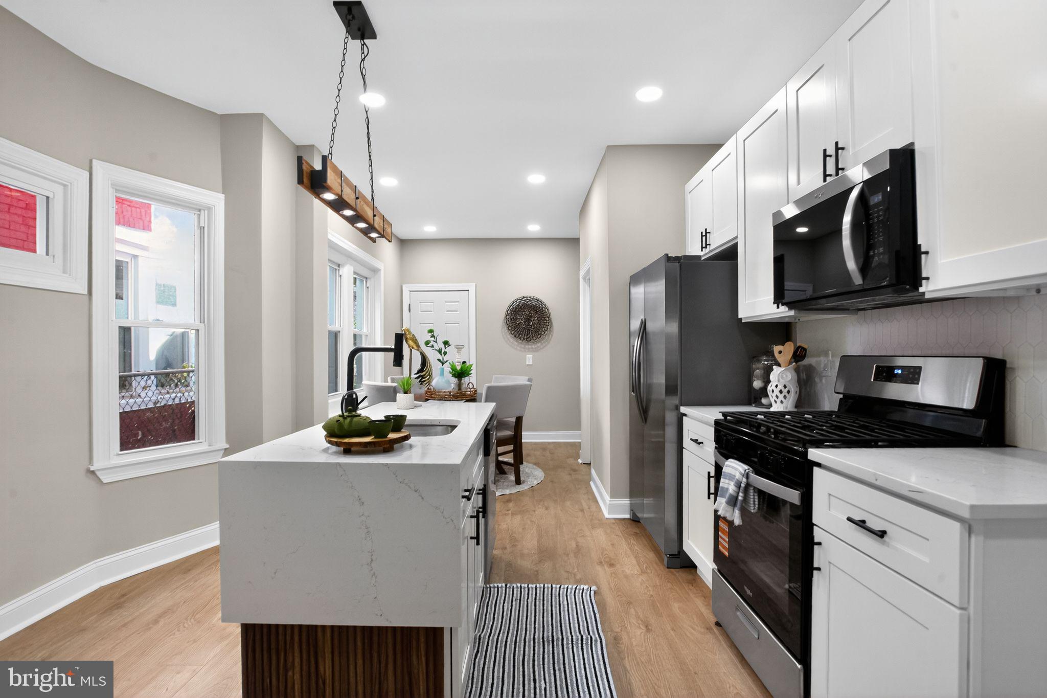 a kitchen with stainless steel appliances kitchen island granite countertop a refrigerator a sink dishwasher a stove and a dining table with wooden floor