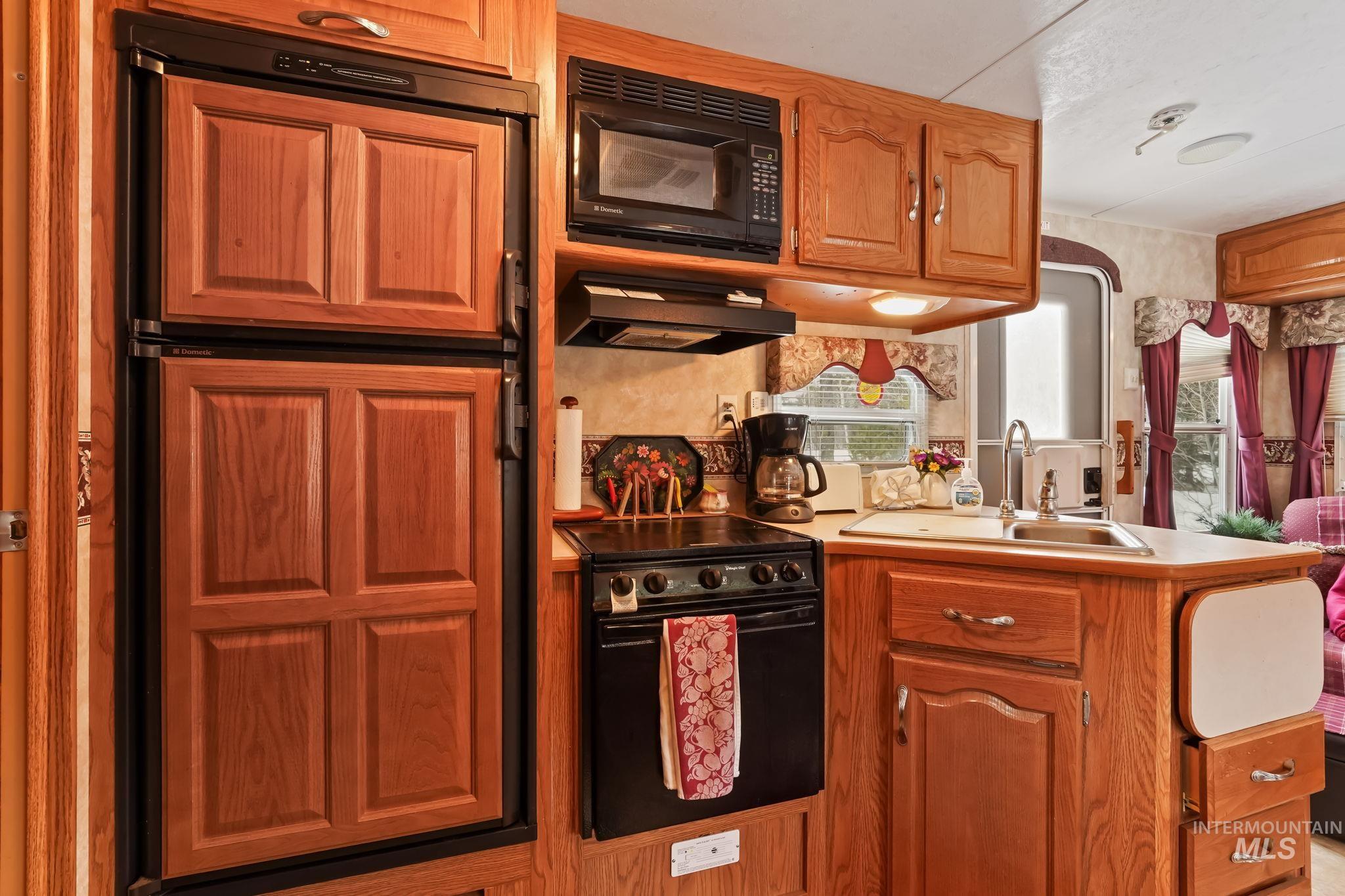 881 West Roseberry Road Donnelly, ID 83615 - Photo 21 of 24 Kitchen with black appliances, wood finish cabinetry, light countertops, and a peninsula
