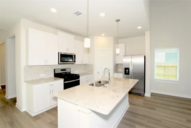 a kitchen with stainless steel appliances kitchen island granite countertop a refrigerator a sink a stove and oven with wooden floor