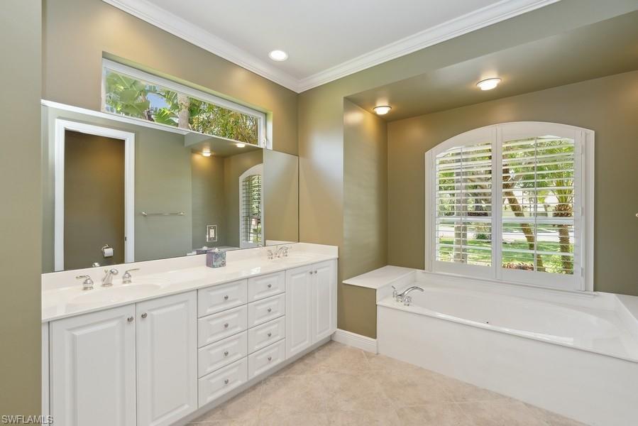 502 Cormorant Cove Naples, FL 34113 - Photo 17 of 25 a spacious bathroom with a double vanity sink a large mirror a bathtub and next to a window