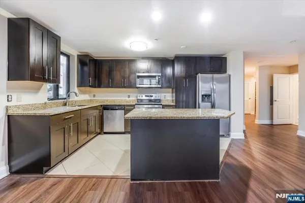 a kitchen with stainless steel appliances granite countertop a stove a sink dishwasher a refrigerator and white cabinets with wooden floor