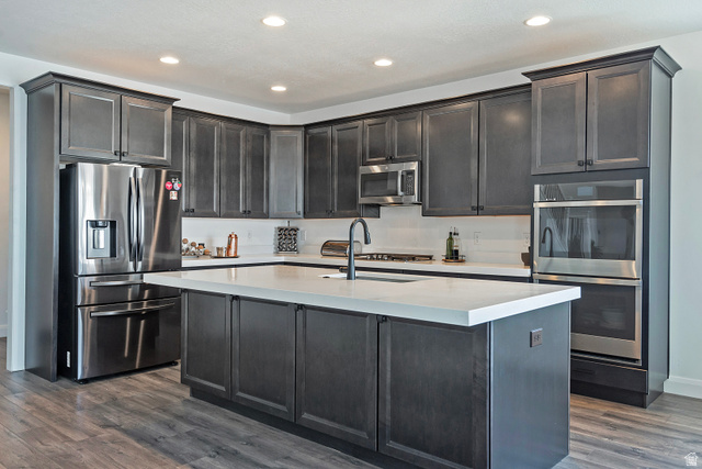 11694 Engelmann Drive Draper, UT 84020 - Photo 18 of 41 Kitchen featuring stainless steel appliances, dark wood-style floors, recessed lighting, a kitchen island with sink, and light stone counters