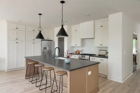 a kitchen with stainless steel appliances granite countertop a stove a sink a refrigerator and chairs with wooden floor