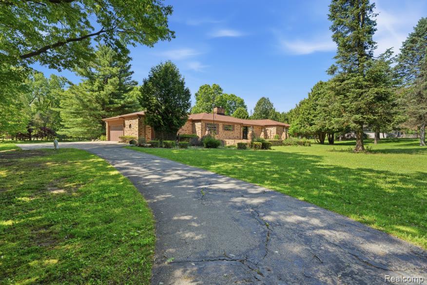 Brick exterior residence with an attached garage, a paved driveway, and expansive lawn areas