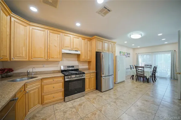 a kitchen with stainless steel appliances granite countertop a stove a refrigerator a sink a dining table and chairs with wooden floor