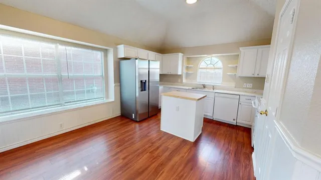 a kitchen with stainless steel appliances granite countertop a refrigerator a sink dishwasher a stove and white countertops with wooden floor