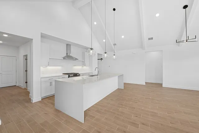 a large white kitchen with a stove a sink a refrigerator and white cabinets with wooden floor