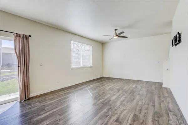 an empty room with wooden floor ceiling fan and windows