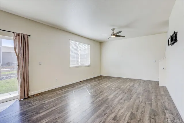an empty room with wooden floor ceiling fan and windows