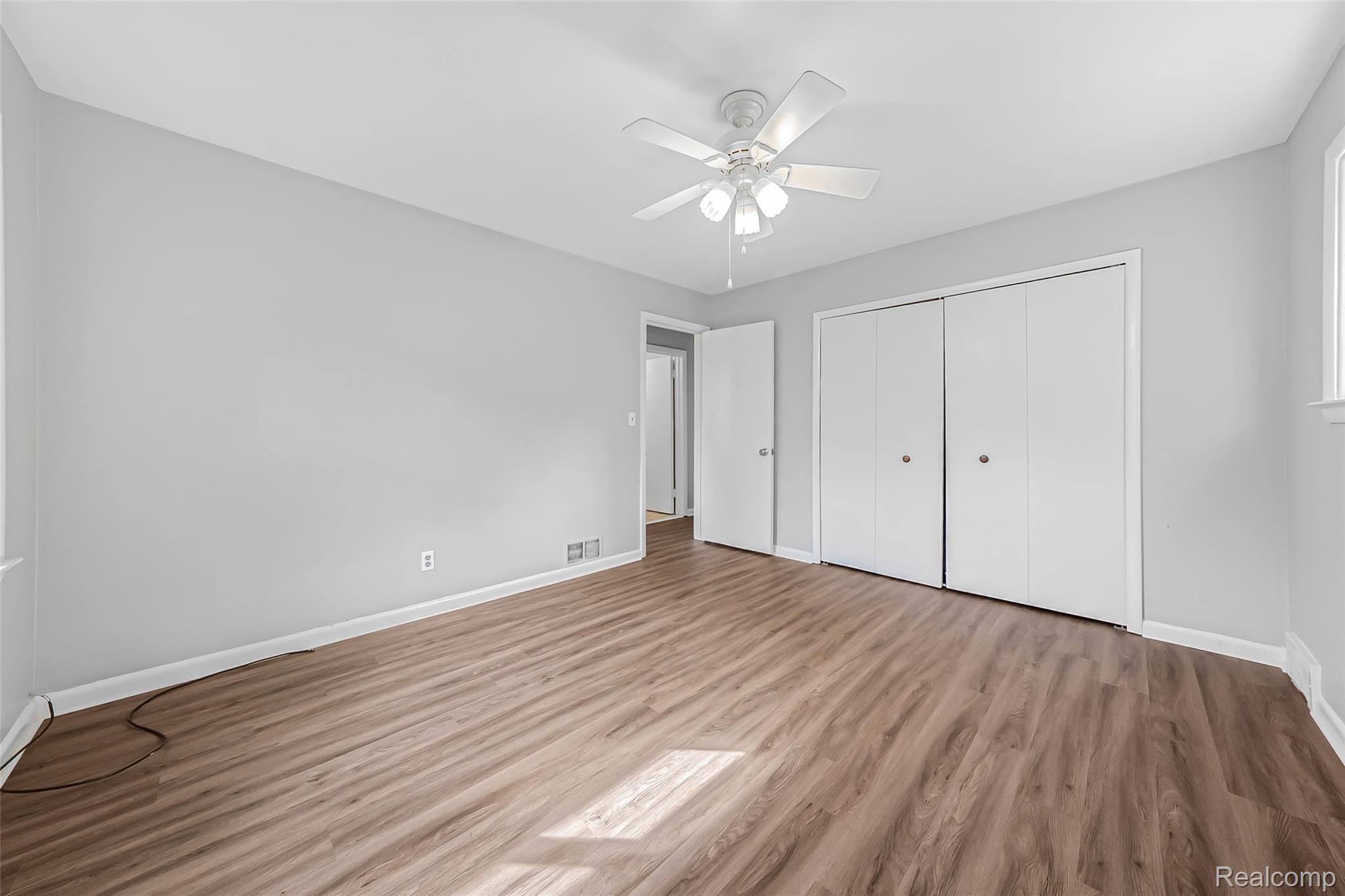 2329 Rutherford Road Bloomfield Hills, MI 48302 - Photo 15 of 46 Spacious room featuring wood-finish flooring, light grey walls, a ceiling fan with integrated lighting, and multiple closet doors