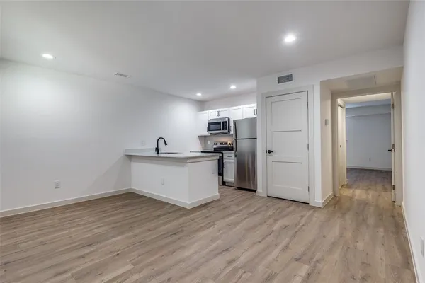 a view of an empty room and kitchen with wooden floor