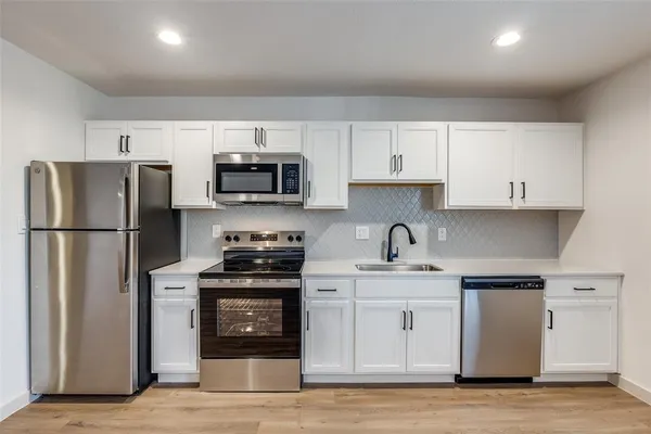 a kitchen with stainless steel appliances granite countertop a refrigerator stove a sink and white cabinets
