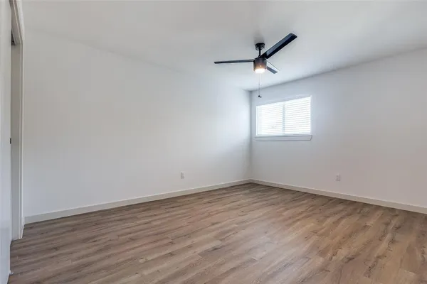 an empty room with wooden floor ceiling fan and windows