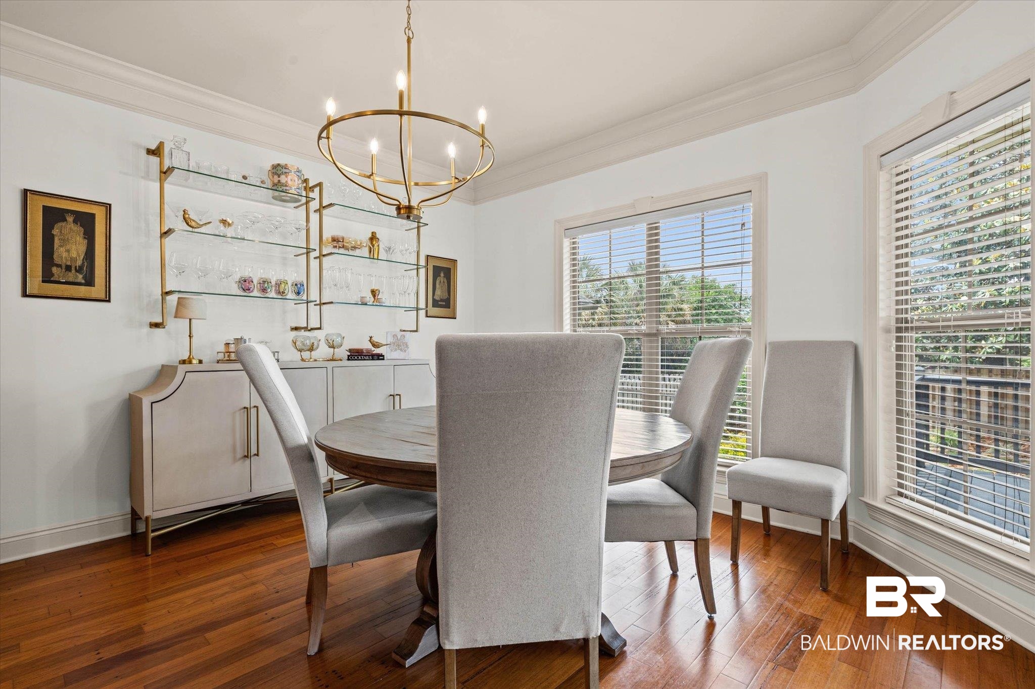 3459 Rue Royal Mobile, AL 36693 - Photo 11 of 31 Room featuring wood-finish flooring, a wall-mounted shelving unit with glass shelves and brass-tone framing, an overhead brass-tone chandelier, and multiple windows with blinds