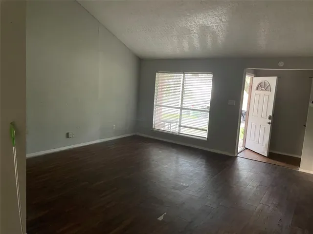 an empty room with wooden floor and windows with curtains