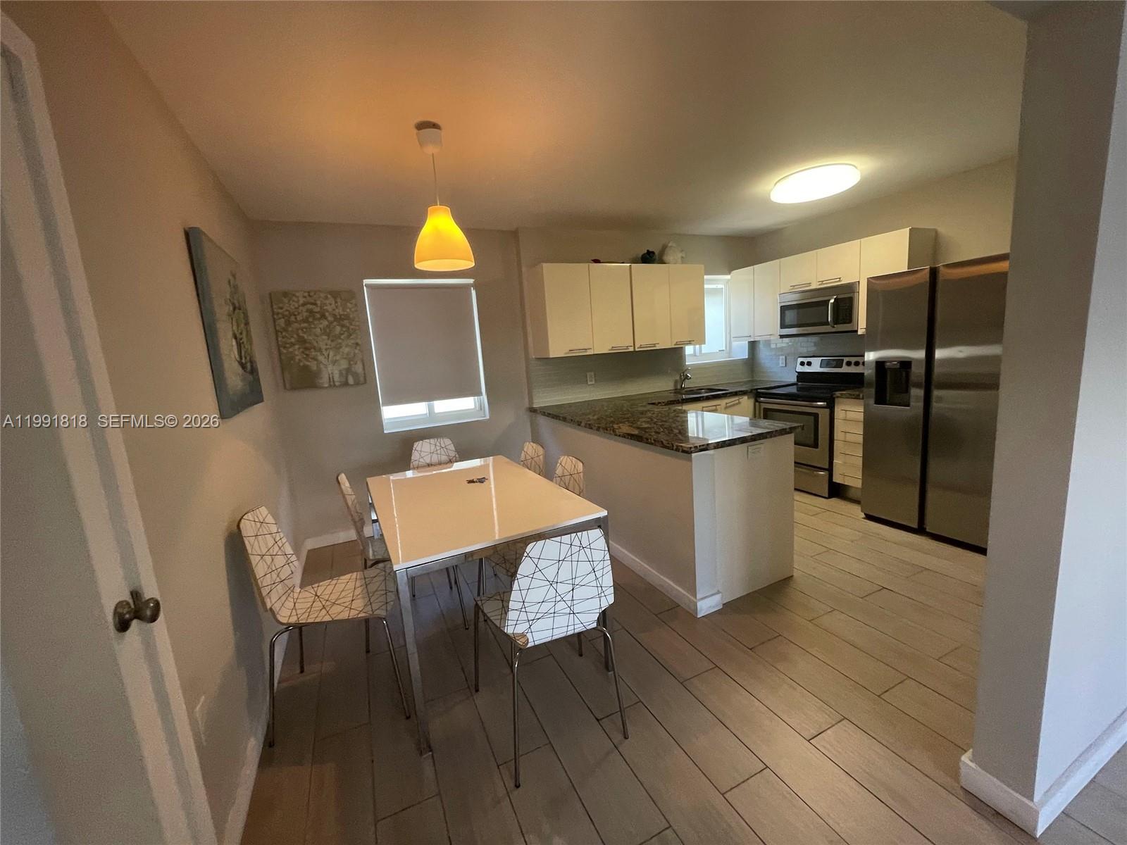 625 77th Street, Unit 2 Miami Beach, FL 33141 - Photo 7 of 17 a kitchen with stainless steel appliances granite countertop a refrigerator a stove a sink a dining table and chairs with wooden floor