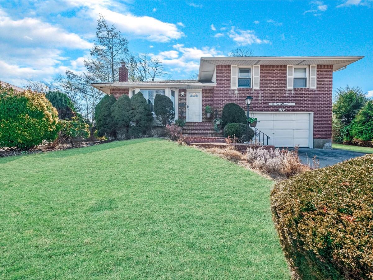 Tri-level home with a garage, driveway, a chimney, a front lawn, and brick siding