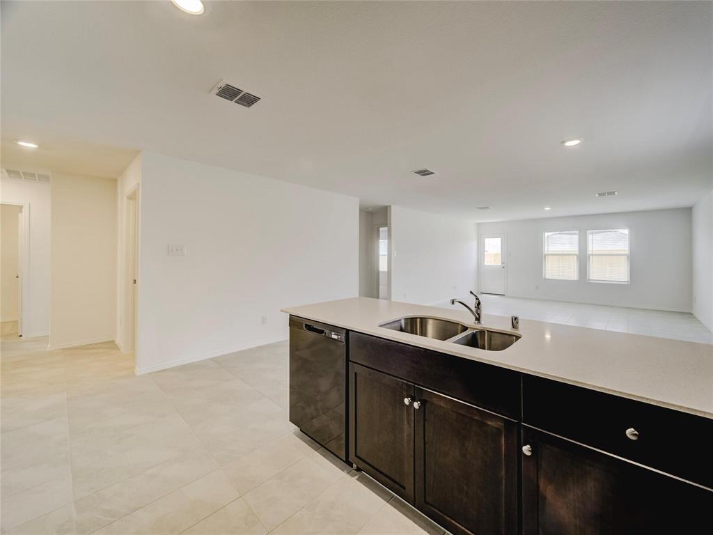 357 Sun Bluff Road Fort Worth, TX 76052 - Photo 7 of 35 Kitchen island featuring a dual basin stainless steel sink with a chrome faucet, dark wood cabinetry, and light-colored countertops